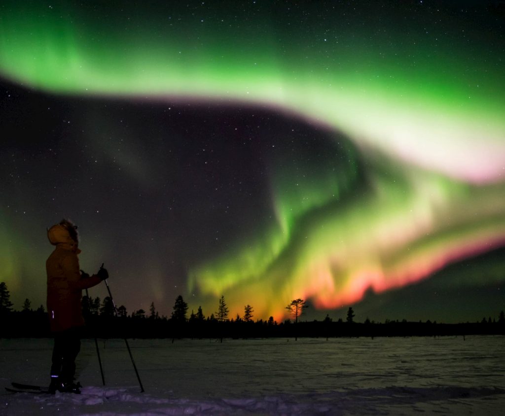 Person wathcing colourful northern lights above the frozen lake in lapland